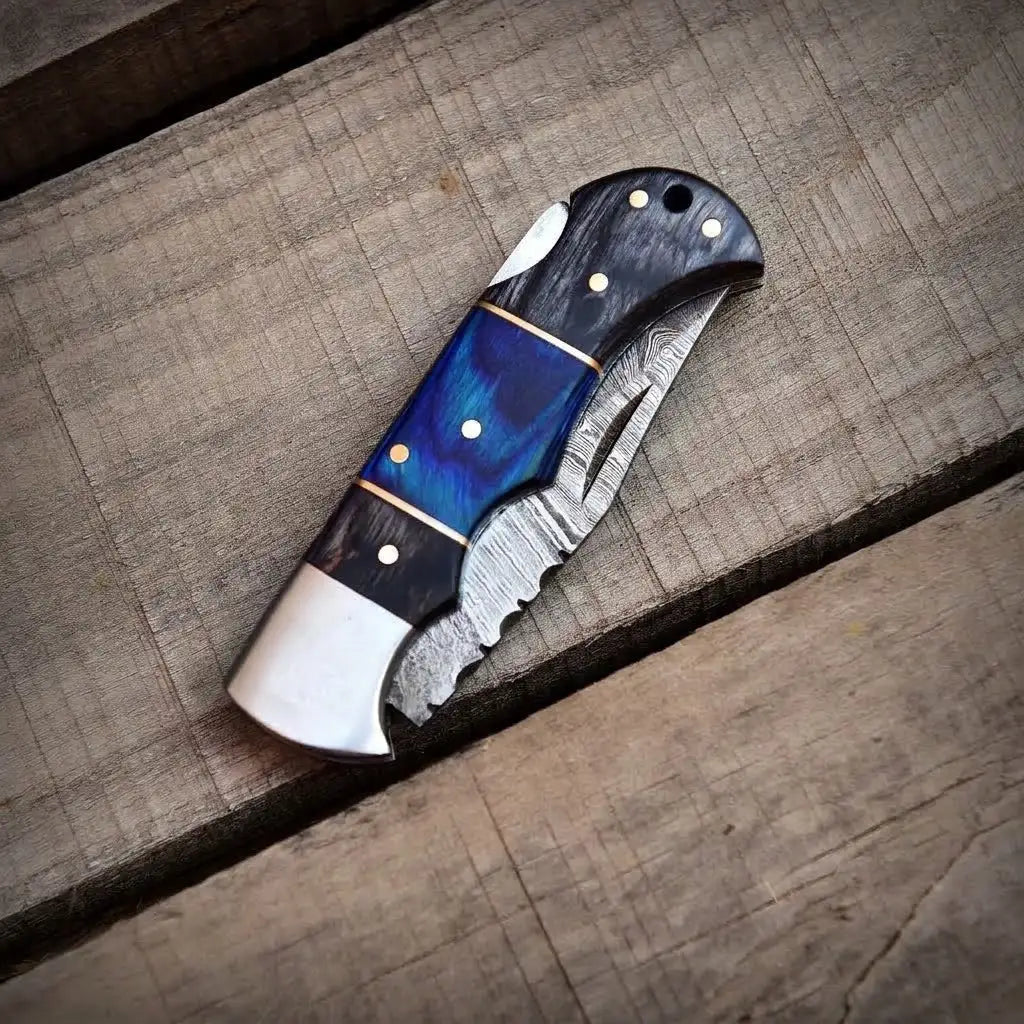 Closed handmade Damascus steel folding pocket knife with a dark blue wood handle resting on a wooden surface.