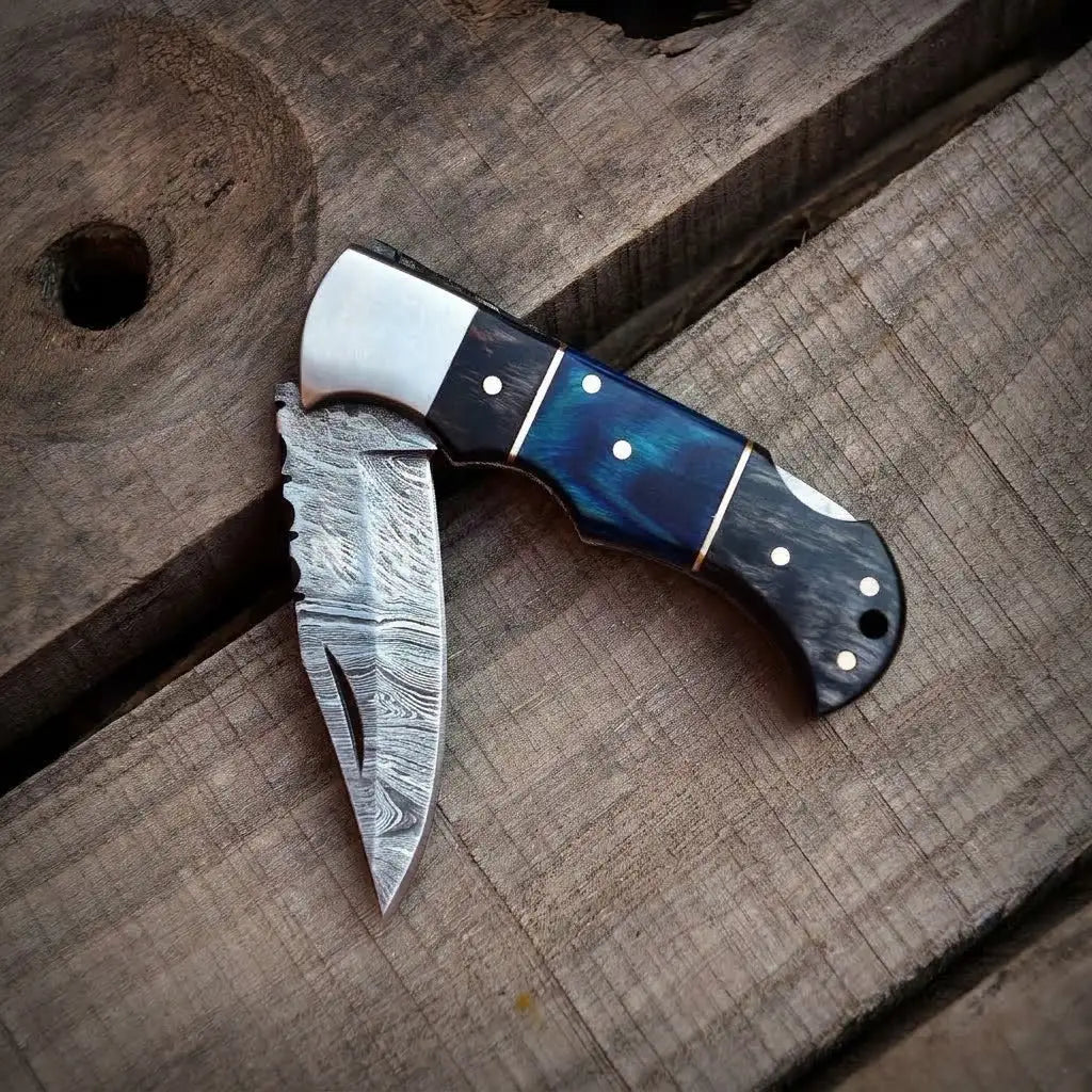 Half-open handmade Damascus steel pocket knife showing filework blade detail and a blue resin wood handle.